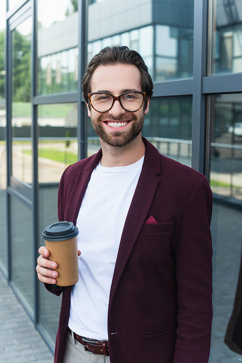 Smiling businessman with coffee to go smiling at camera near building outdoors