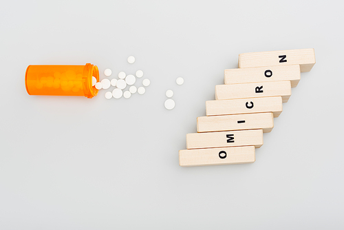 top view of container and pills near wooden bricks with omicron lettering on grey background