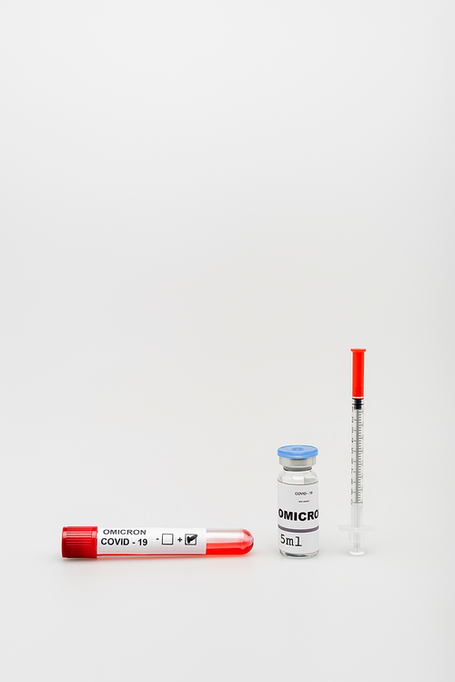 test tube with positive result near covid-19 omicron variant vaccine and syringe on grey background