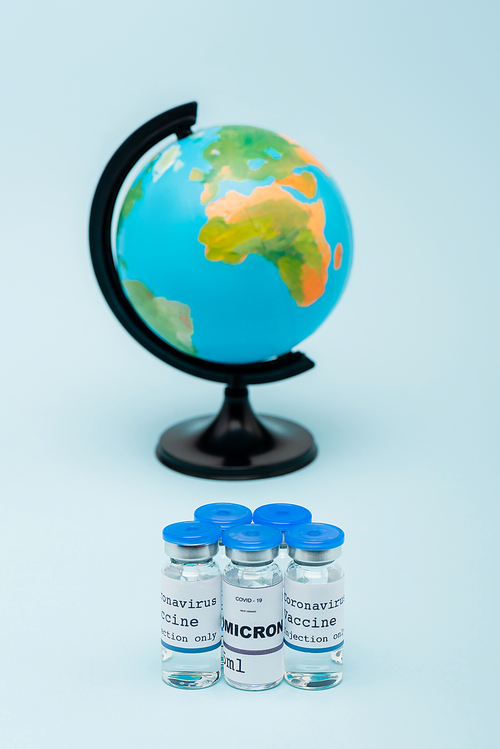 covid-19 omicron variant vaccine bottles near blurred globe on blue background