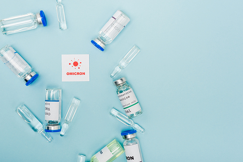 top view of vaccine vials and ampoules near card with omicron lettering and bacteria on blue