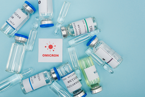 top view of white card with red omicron lettering and bacteria near vaccine vials and ampoules on blue