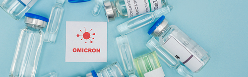 top view of card with red omicron lettering and bacteria icon near vaccine bottles and ampoules on blue, banner