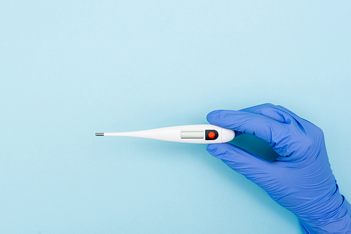 partial view of doctor in latex glove holding electronic thermometer on blue