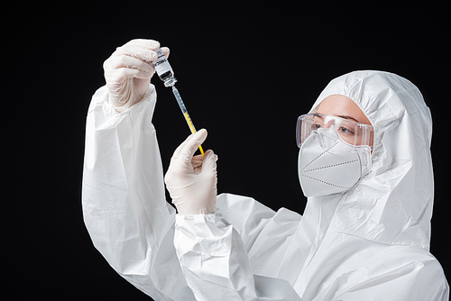 immunologist in personal protective equipment holding syringe and covid-19 omicron variant vaccine isolated on black