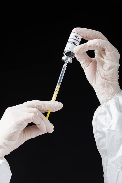 partial view of immunologist in white latex gloves holding syringe and omicron variant vaccine isolated on black