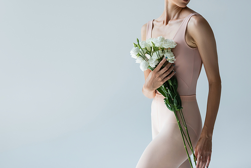 cropped view of young ballerina holding bouquet of flowers isolated on grey