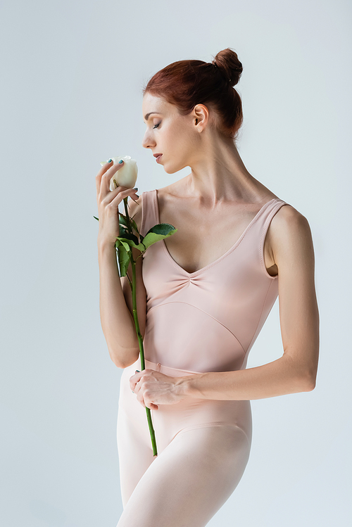 redhead ballerina with closed eyes smelling rose isolated on grey