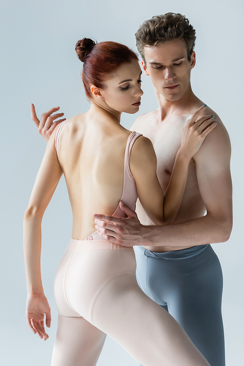 elegant ballerina dancing with shirtless partner isolated on grey