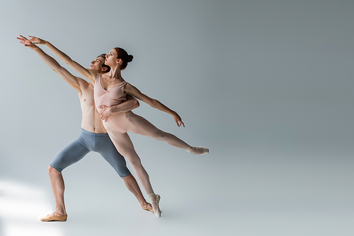 full length of shirtless man and sensual woman with outstretched hands performing ballet dance on grey