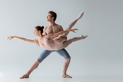 shirtless ballet dancer lifting young ballerina isolated on grey