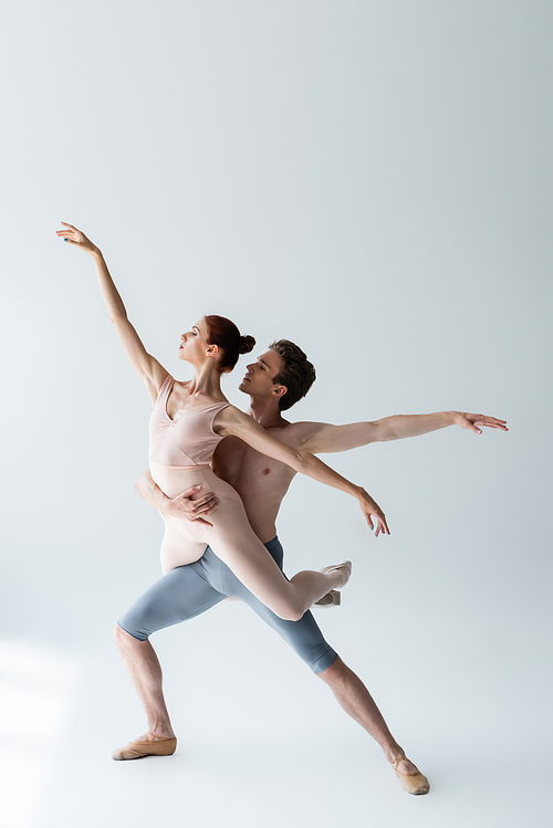 full length of shirtless man and flexible woman in bodysuit performing ballet dance on grey