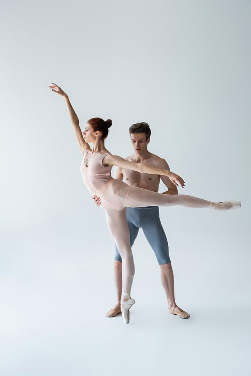 full length of shirtless man and flexible woman performing ballet dance on grey