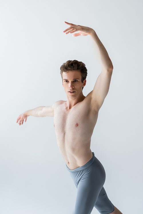 young and shirtless ballet dancer performing ballet dance isolated on grey