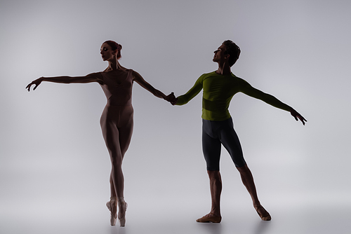 silhouette of young dancer holding hands with ballerina on grey