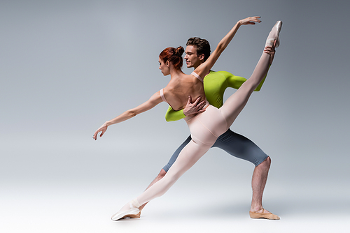 full length of man and flexible woman performing ballet dance on grey