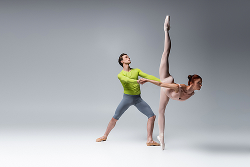 full length of ballet dancer supporting ballerina during dance on dark grey