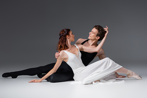 graceful ballerina in white dress dancing with partner on dark grey