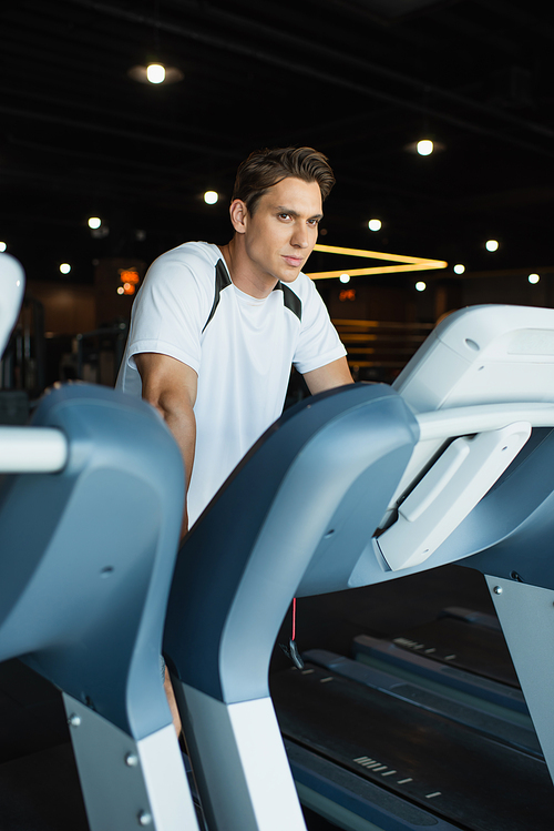 sportive man looking away while standing on treadmill in gym