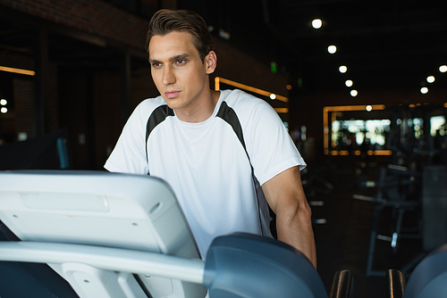 man looking away while standing on treadmill in sports center