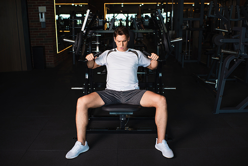 full length view of athletic man working out on arm extension exercising machine in gym