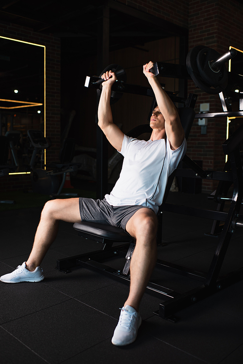 full length view of man in sportswear training on arm extension exercising machine