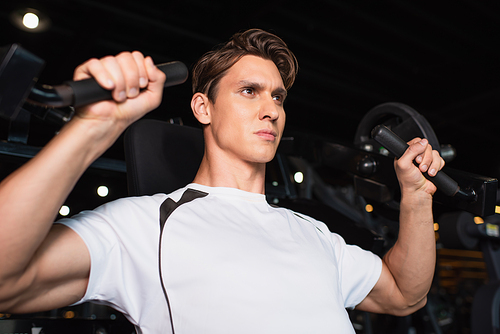 sportive man looking away while working out on arm extension exercising machine