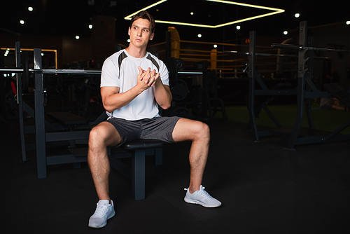 full length view of man in sportswear sitting on exercising machine and warming up hands