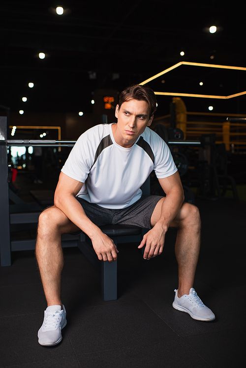 full length view of athletic man looking away while sitting on exercising machine in gym