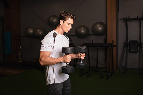 athletic man in sportswear exercising with dumbbells in gym