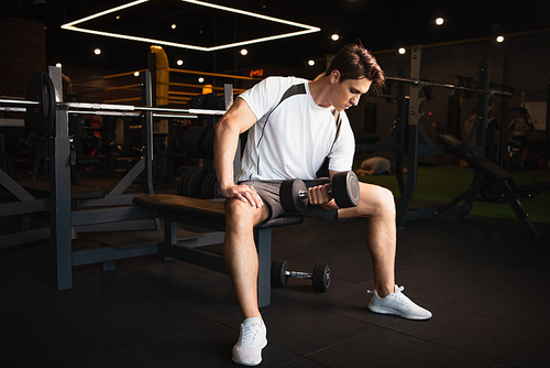 full length view of sportsman training with dumbbell in sitting pose