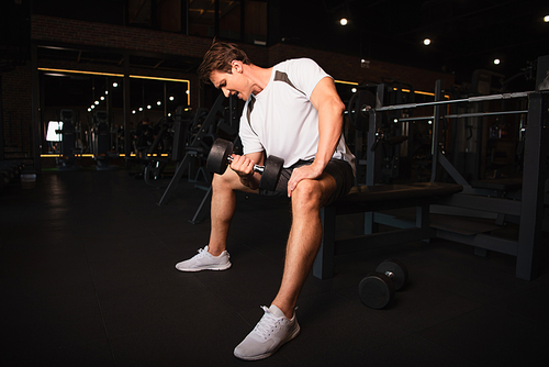 full length view of athletic man in sportswear training with dumbbell in gym