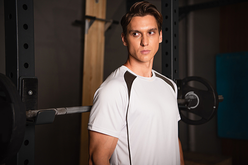 sportive man looking away while standing near weightlifting exercising machine in gym