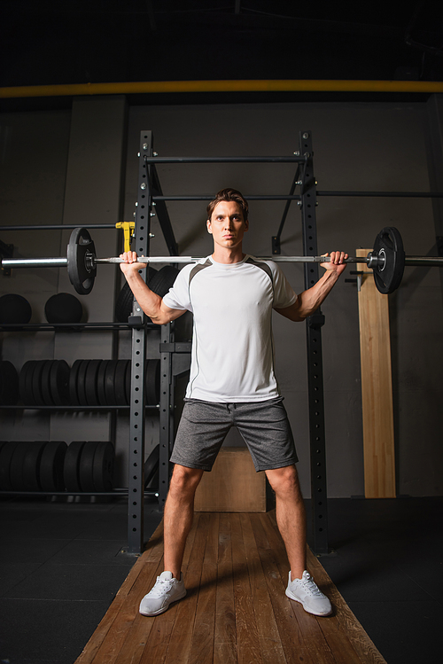 full length view of man in sportswear training with barbell in gym