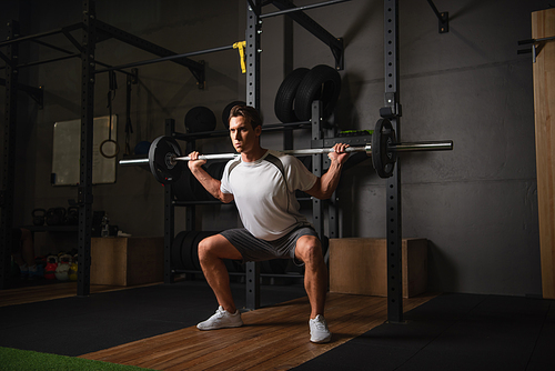 full length view of athletic man exercising with barbell in sports center