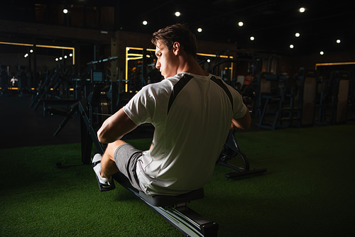back view of man training on pull rope exercising machine in sitting pose