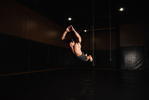 barefoot and shirtless gymnast jumping while training in gym