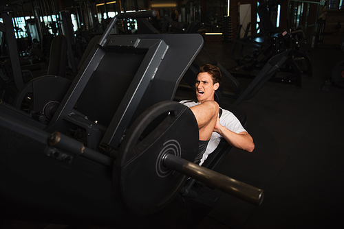 sportsman shouting while working out on leg extension exercising machine in sports center