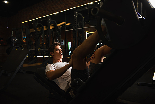 athletic man working out on leg extension exercising machine in sports center