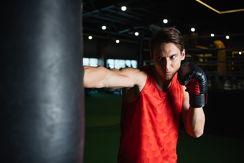 athletic man training with punching bag in sports center on blurred foreground