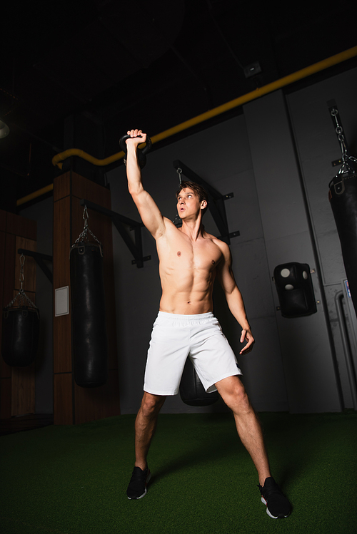 full length view of shirtless muscular sportsman exercising with kettlebell in gym
