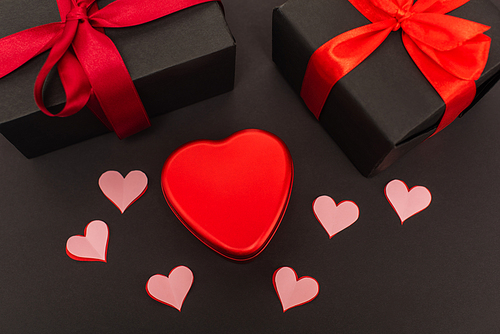 top view of paper cut hearts and metallic box near wrapped presents on black