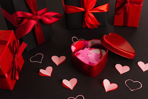 paper cut hearts near metallic box and wrapped presents on black
