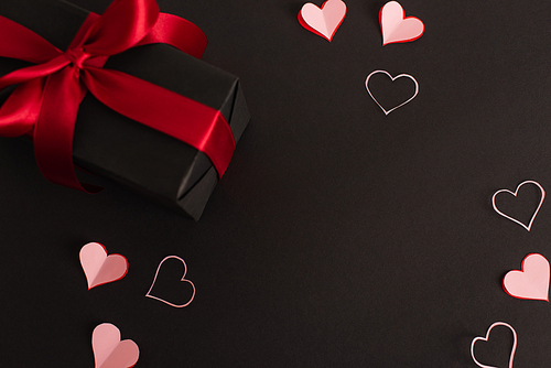 top view of pink paper cut hearts near wrapped present on black