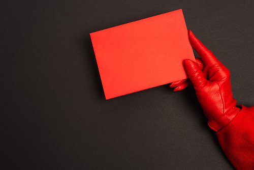 cropped view of person in red glove holding envelope on black