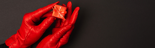 cropped view of woman in red gloves holding tiny gift box on black, banner
