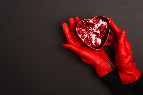cropped view of woman in red gloves holding metallic heart-shaped box on black