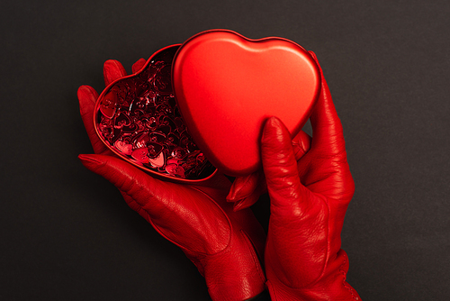top view of woman in red gloves holding metallic heart-shaped box on black