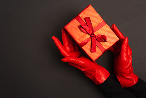 cropped view of woman in red gloves holding wrapped present on black