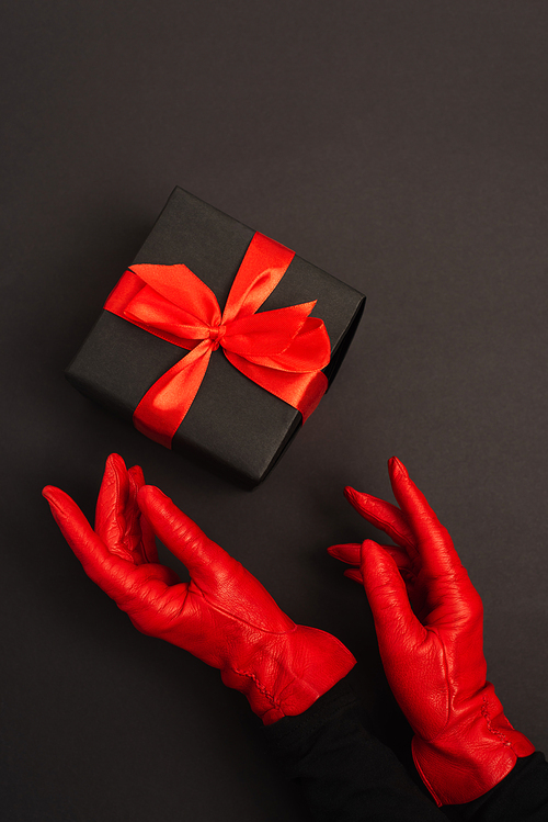 cropped view of woman in red gloves reaching wrapped present on black